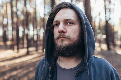 Young man looking away while standing against trees in forest