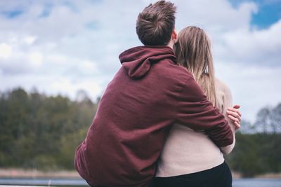 Rear view of couple embracing while sitting against cloudy sky