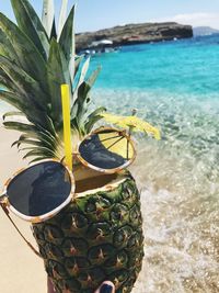 Close-up of sunglasses on pineapple with drink at beach