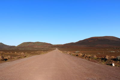 Road amidst desert against clear blue sky