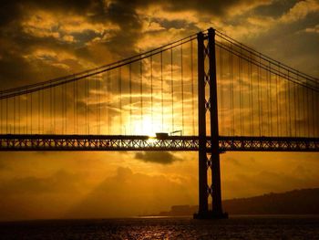Silhouette bridge against calm sea at sunset