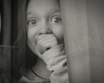 Close-up portrait of surprised girl with hand covering mouth by curtain