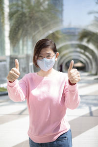 Woman wearing protection mask standing outdoor raising hand for good healthy