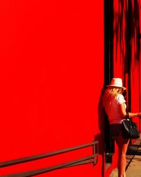Rear view of woman leaning on red wall