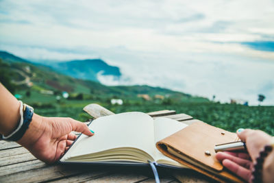 Midsection of woman reading book against landscape