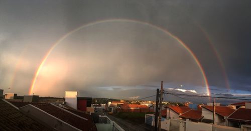 Rainbow over city against sky during sunset