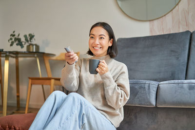 Young woman using mobile phone while sitting on sofa at home