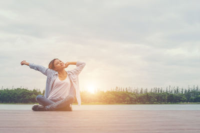 Woman stretching hands on pier against lake