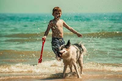 Shirtless boy with dog standing in sea against sky during sunny day