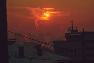 Silhouette factory against sky during sunset