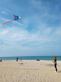 Woman flying kite at beach against sky