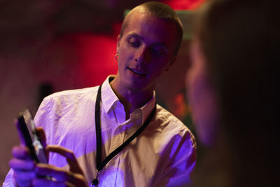 Young businessman sharing mobile phone with colleague in illuminated workshop