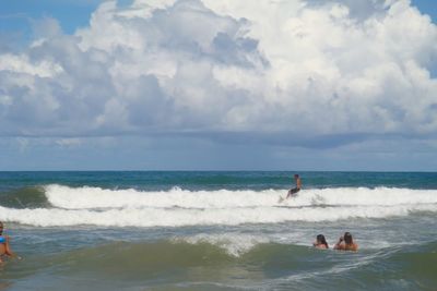 Waves splashing on beach against cloudy sky