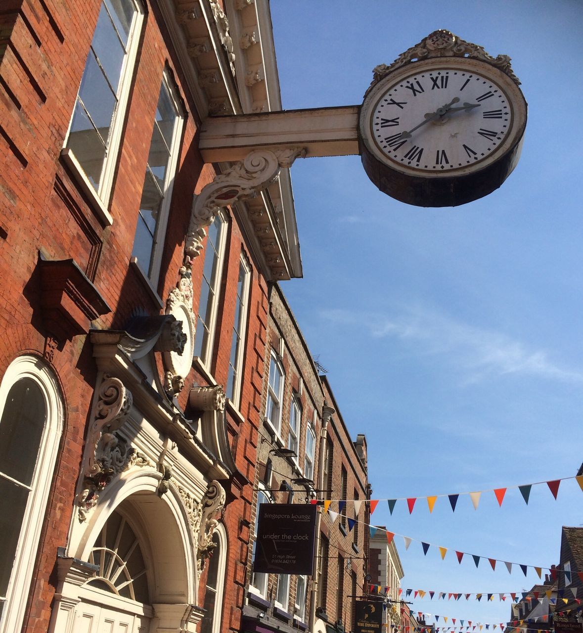 low angle view, architecture, built structure, building exterior, clock, time, sky, clock tower, window, day, clear sky, text, building, outdoors, high section, clock face, no people, flag, communication, arch