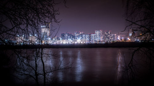 Illuminated buildings by river against sky at night