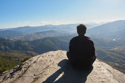 Rear view of man standing on mountain against sky