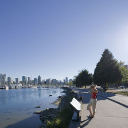 Side view full length of woman standing by lake at stanley park in city on sunny day