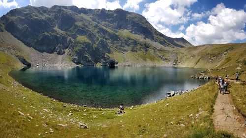 People on lake by mountains against sky