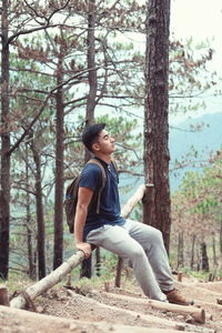 Side view of young man sitting on railing in forest