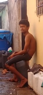 Side view of shirtless young man sitting on wall