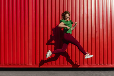 Full length of woman jumping on red wall