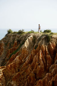 Man standing on rock by sea against clear sky