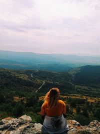 Rear view of woman sitting at the edge of mountain against sky
