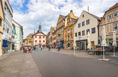 People on street amidst buildings in city against sky