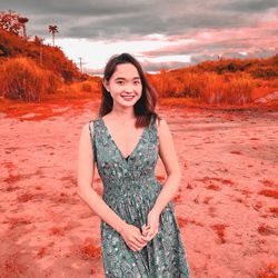 Portrait of smiling young woman standing against sky during sunset