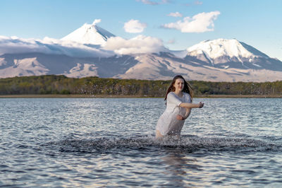 Young woman standing in lake against snowcapped mountain