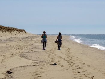 Rear view of two women walking on beach against clear sky