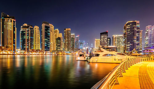 Illuminated buildings by river against sky at night