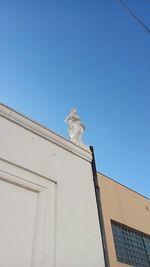 Low angle view of bird perching on building against blue sky