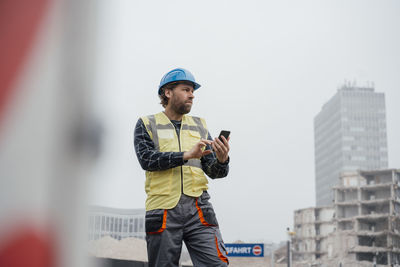 Smiling mature worker with smart phone at construction site