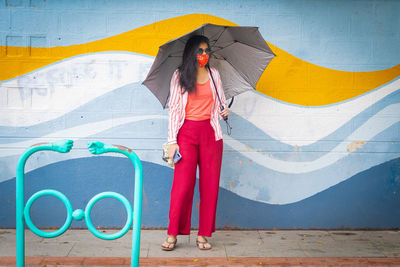 Woman with umbrella standing against graffiti wall