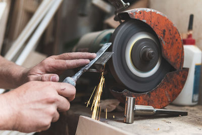 Male carpenter sharpening chisel using grinder in workshop