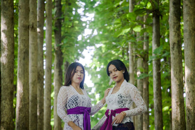 Woman standing by tree trunk in forest