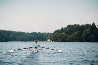 Man rowing boat in lake against sky