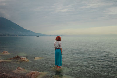 Rear view of woman standing at sea shore against sky