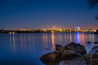 Illuminated buildings by sea against sky at night