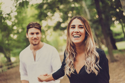 Portrait of smiling young couple standing against trees