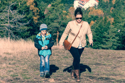 Full length of mother and son walking on field