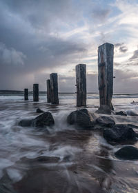 Wooden posts in sea against sky