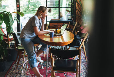 Young smiling blonde woman freelancer in yellow headphones working on laptop on the table at cafe