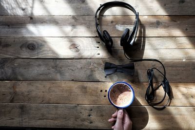 Cropped hand of person holding coffee cup on wooden table by headphone