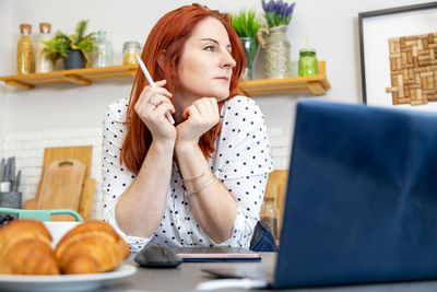 Young woman looking away while sitting on table at home