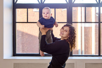 Portrait of mother holding baby mid-air by window