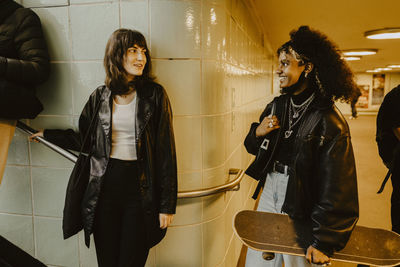 Smiling female friends looking at each other in illuminated subway