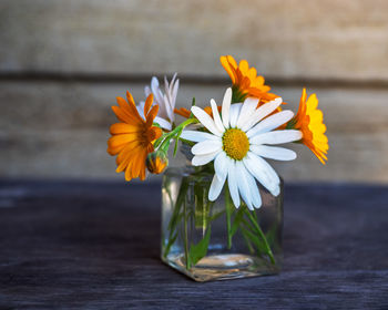Small bouquet with chamomiles and calendula in a glass jar on the table of a country house