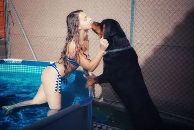 Side view of young woman kissing dog from swimming pool